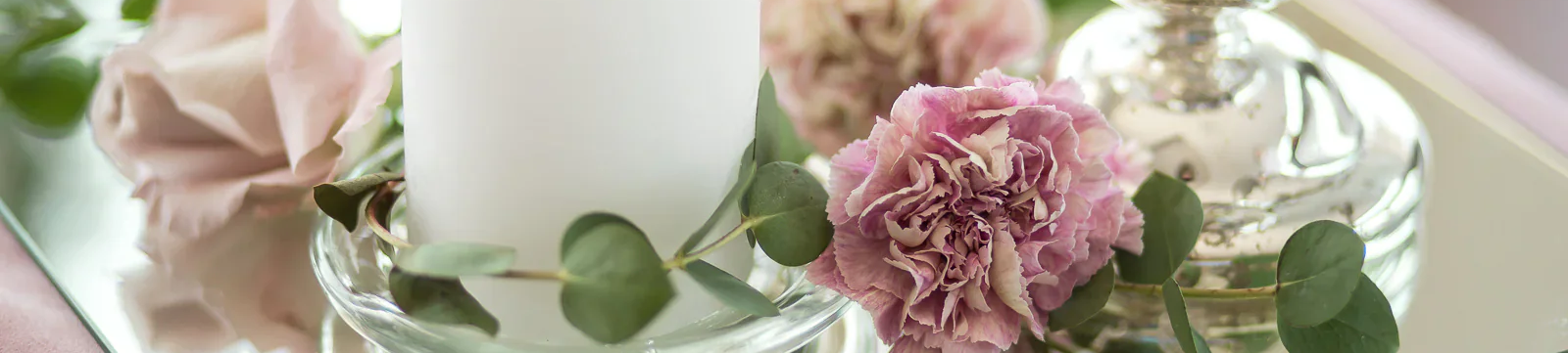 White pillar candle on a glass tray with pink carnations and eucalyptus greenery